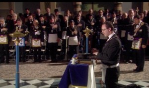 Man praying at altar with 3 books of scripture.  Notice the different aprons of people in the background.